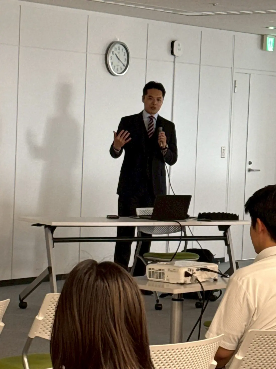 近藤が手のひらを大きく広げるジェスチャーで語りかける様子。受講者は後ろ姿が中心。